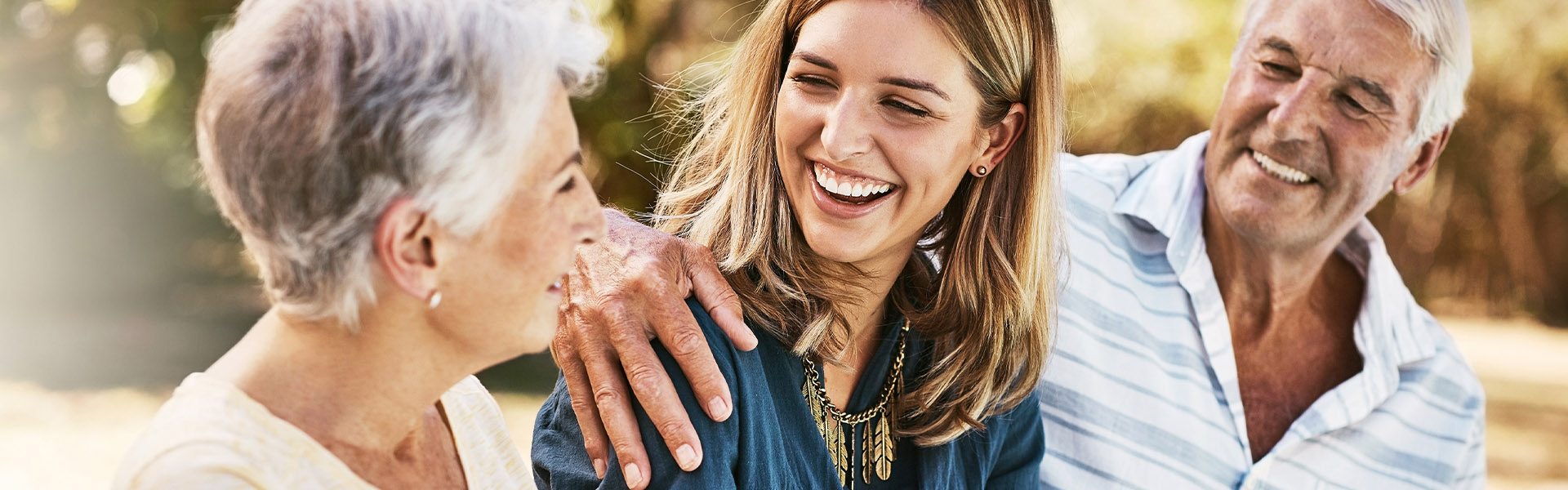 Oma und Opa haben ihre Enkelin zwischen sich und genießen einen sonnigen Tag draußen.