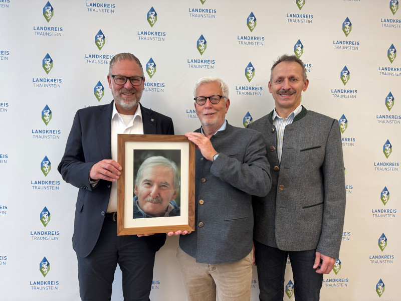 Landrat Andreas Danzer (li.) bedankt sich gemeinsam mit Florian Seestaller, Leiter der Bürgerhilfsstelle im Landratsamt Traunstein (re.), bei Peter Schimpf, Vorstand der Georg Johannes Hipp-Stiftung (Mi.), für die großzügige Spende in Höhe von 20.000 Euro. Das Foto zeigt die drei bei der Spendenübergabe im Landratsamt Traunstein – mit einem Porträt des Stifters Georg Johannes Hipp, dessen Engagement für Menschen in Not fortgeführt wird.